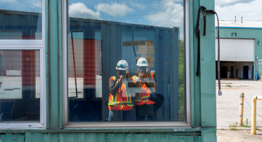 Two photographers in construction safety equipment taking a picture of themselves in a window.