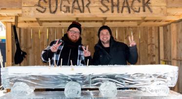 two people at an outdoor booth in front of large block of ice