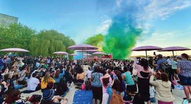 A crowd on a beach with a smoke sculpture in background.