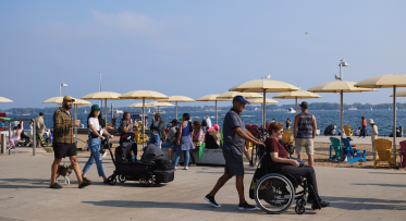 People at a beach on a summer day. One person is using a wheelchair, another is pushing a stroller. 