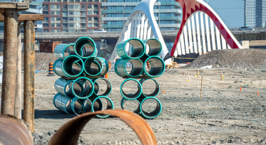 Blue pipes stacked in front of a bridge in a construction site.