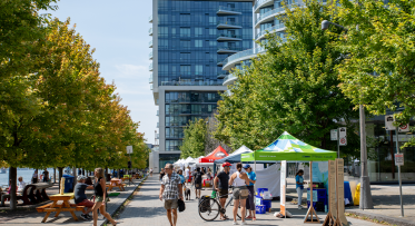 People enjoy a market along a promenade on the waterfront.