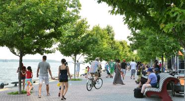 people strolling, cycling and sitting along a tree-lined water's edge