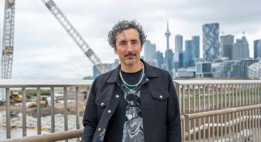 An individual dressed in black poses for the camera with Toronto's Skyline overlooking CN Tower in the backdrop.