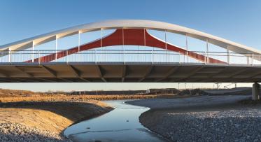 A modern bridge over a water body with concrete on the sides and sky in the background.