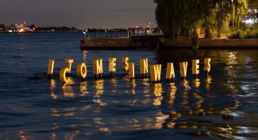 Letter IT COMES IN WAVES float and glow on water in the dark as part of a floating artwork.