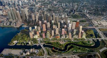 Aerial view of artist rendering showing a new island community on Toronto's waterfront with a winding river., green space, and developments.