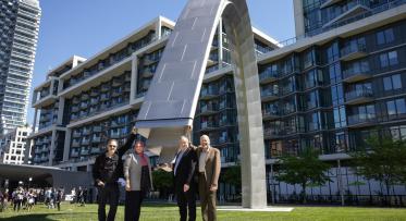 Four people pose next to a large arch - public art installation at the official unveiling in Sherbourne Common.