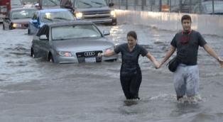 cars stuck and people walking through flooded streets